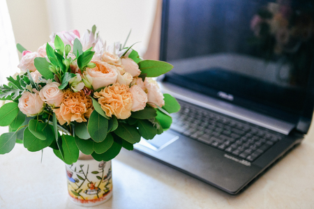 delicate wedding bouquet of roses carnations is on the table near the laptop. bridal bouquet, floral arrangementの写真素材