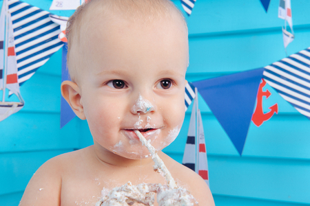 decoration for the boys birthday, smash the cake in a nautical marine style. stylized birthday ship photo shoot. Cheerful boy eats and break a cake with his hands on the first holidayの写真素材