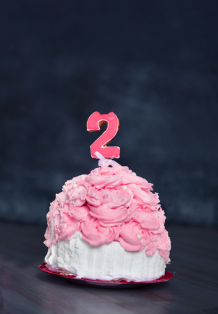 themed birthday for a fun emotional girl of the blonde smash the cake in pink color on a black background. stylized photo session tradition with sweet decor and balloonsの写真素材