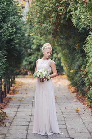 beautiful elegant blonde bride is standing in a park on the road with an unusual autumn bouquetの写真素材