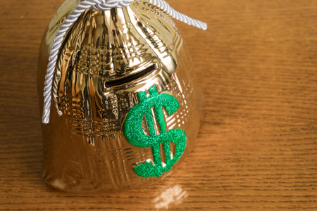 piggy bank looks like a golden bag of money is on the table and the hand throws a coin there. close-upの写真素材