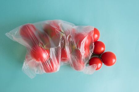 branch of ripe cherry tomatoes lies in a plastic bag on a blue contrasting backgroundの写真素材