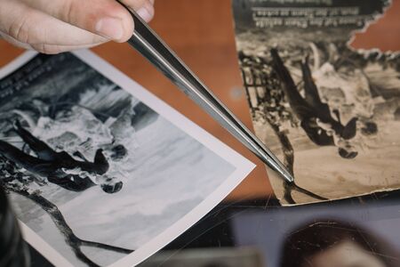 Belarus, Soligorsk, July 1, 2019: mastery of restoring old vintage damaged photos of close-up specialist working place with a pair of tweezersのeditorial素材