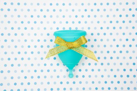 blue menstrual cup with gold bow as a gift on a white background with blue polka dots. feminine hygiene during the period, top viewの写真素材