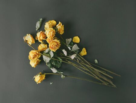 A dry bouquet of yellow roses on a black background, frustration at the end of the holidays, a sad day, toned faded faded image stylized retroの写真素材