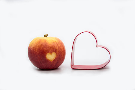 Red Juicy apple with a heart shape cut-out and heart shaped cookie cutter. Isolated on white backgroundの写真素材