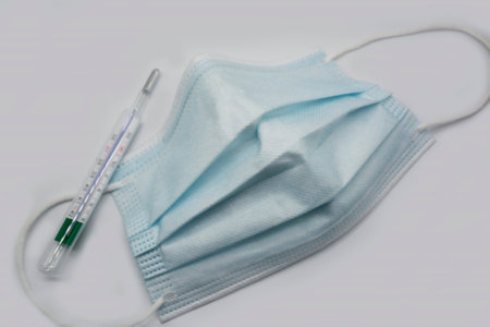 Blue surgical protective medical face mask, thermometer isolated on white background. Top view.