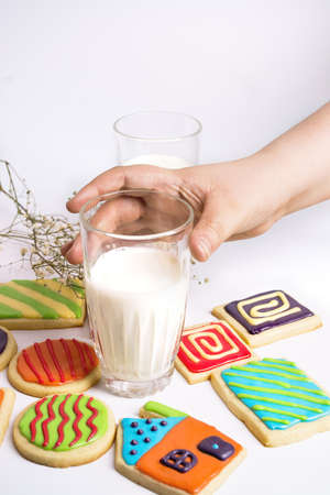 hand holding glass of milk. Colorful cookies placed next to it on the table on white background.の写真素材