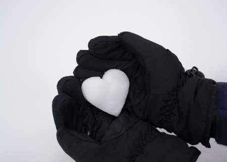 Hands in black gloves holding white snow heart. Selective focus, top view.