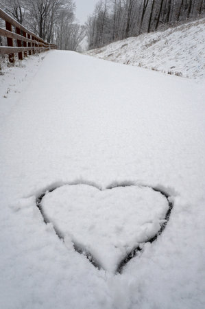 Big heart drawn on snow in park with long path ahead. Love symbol on snowの写真素材