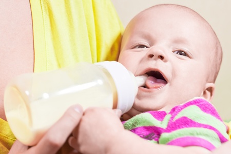 Little smiling baby and bottle on the hands of his motherの写真素材