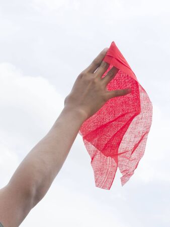 Human hand holding red fabric on blue sky background as symbol of stop gestureの写真素材