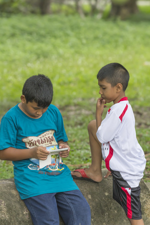 NAKHON SI THAMMARAT, THAILAND - OCTOBER 18: Unidenfied Asian Thai boys enjoy playing games on the smart phone at park on October 18, 2014 in Nakhon Si Thammarat province, Thailand.のeditorial素材