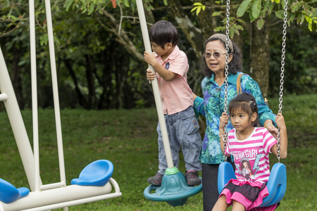 NAKHON SI THAMMARAT, THAILAND - OCTOBER 18: Asian Thai grandmother pushing kids on swing in playground on October 18, 2014 in Nakhon Si Thammarat province, Thailand.のeditorial素材