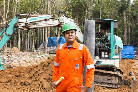 NAKHON SRI THAMMARAT THAILAND  MAY 10: Thai worker wearing high safety jacket standing and watching bucket digger digging at construction site on May 10 2015 in Nakhon Sri Thammarat Thailand.のeditorial素材