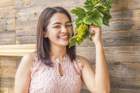 Portrait of pretty young woman holding ripe grapes bunch on wood backgroundの写真素材