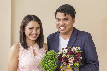 Portrait of Asian young couple holding vase of flowersの写真素材