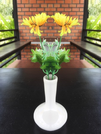 Yellow flower in vase on table over brick wallの写真素材
