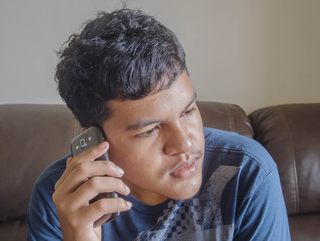 Asian Thai young man sitting on sofa chair and call mobile phone