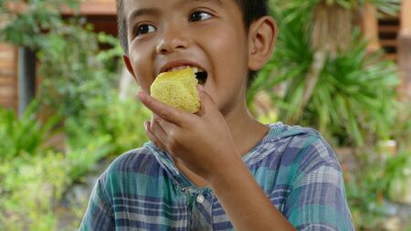 Close-up shot of Asian Thai little boy enjoys eating tasty cakeの写真素材