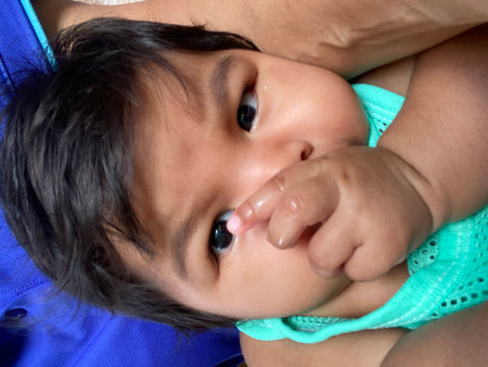 Asian baby girl in a blue dress lying on the floor and sucking her finger