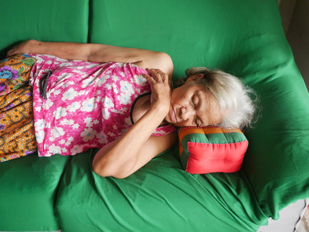 Elderly woman sleeping on a green sofa in her home.の写真素材