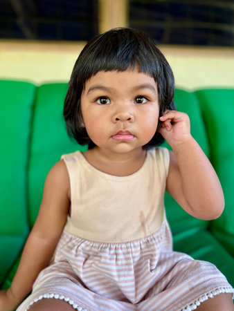 Cute Asian little girl with big eyes sitting on sofa in living room