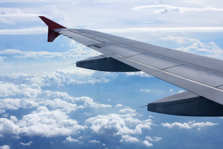 Wing of an airplane flying in the blue sky with white clouds.