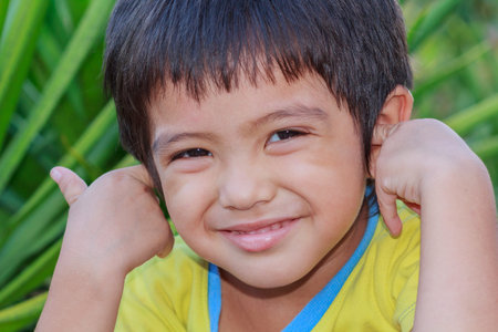 Outdoor portrait head shot of Asian little boy smiling face looking with eyes contact to cameraの写真素材