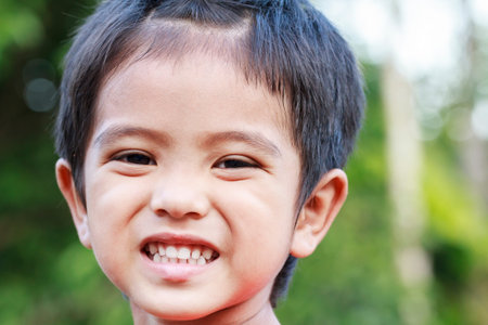 Outdoor portrait head shot of Asian little boy smiling face looking with eyes contact to cameraの写真素材