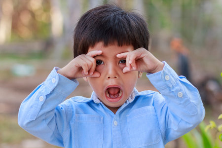 Portrait of happy cute Asian Thai little boy rounding his eyes with his fingersの写真素材