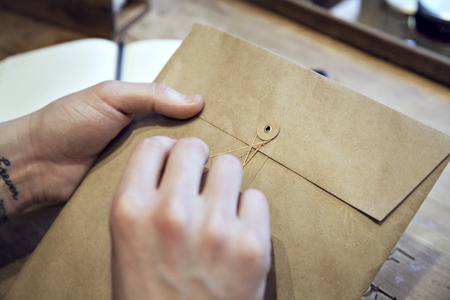Close-up view of male hands holding brown envelope with coffee at the wooden deskの写真素材