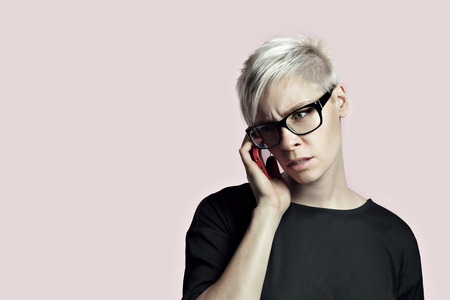 Portrait of blonde woman with smartphone and glasses, short hair pink backgroundの写真素材