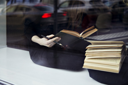 Education concept. close-up of books in hands. Two women near window in a libraryの写真素材