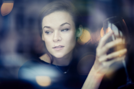 Young woman close-up portrait through window in a restaurant. leisure time with red wineの写真素材
