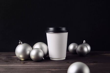 Paper coffee cup and christmas ball on a wooden table. Holiday toys. Silver balls on the background. Happy new year. Hipster cafe. Template for designの写真素材