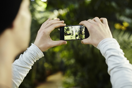 Man taking photo picture by mobile phone in a travel journey, green plants in a park. Fucused on...