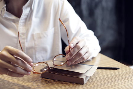 Man hands holding an elegant eyeglasses with horn-rimmed, daylight in a cafeの写真素材