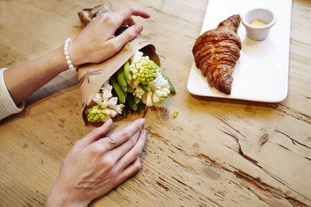 Woman hands with ring on finger, hyacinth bouquet flowers, romantic date in cafe, breakfast with croissant and coffee. St. Valentine's dayの写真素材