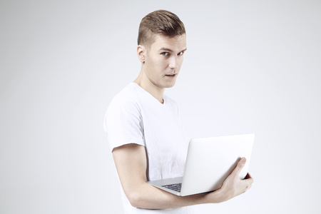 Attractive business man in white t-shirt isolated on white working on laptop. Looking to camera with smiling eyesの写真素材