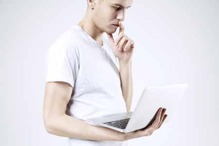 Attractive business man model in white t-shirt isolated on white working on laptop. Thinking with serious face.の写真素材