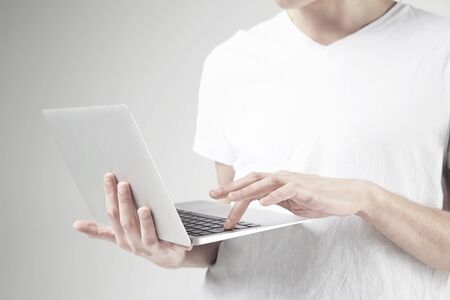 Close-up view of modern laptop in man's hands, guy wearing white t-shirt, working on portable...