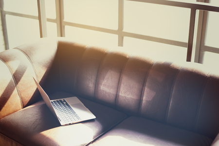 Modern sunny coworking loft office, opened laptop computer on a leather sofa, sunlight through a windowの写真素材