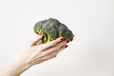 Fresh vegetable broccoli in woman outstretched hand, fingers with red nails manicure, isolated on white background, healthy lifestyle conceptの写真素材