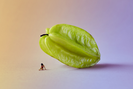 Microworld with woman figure under the carambola tropical fruit on green pink background. Cartoon style, food photographyの写真素材