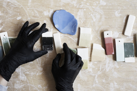 Samples of colored enamel for color ceramic in hands, working process in studio, clay, wood, craft