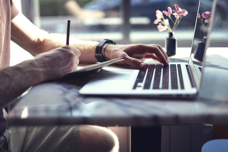 Close-up of manâs hands on laptop. Guy using computer and smartphone sitting in cafe having coffee. Concept of young business people working in public space or co-workingの写真素材