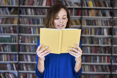 Portrait of woman over 25 in a library reading an opened book, concentrated and smart. Young college student in co-working, concept of studying.の写真素材