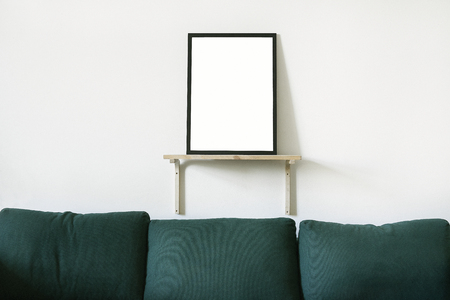 Poster in black frame in white stylish modern interior on a wall above green sofa. Design template mockup.の写真素材