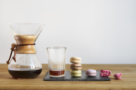 Fresh coffee alternative brewing, sweet brownie cookies on wooden table. White wall behind space for...